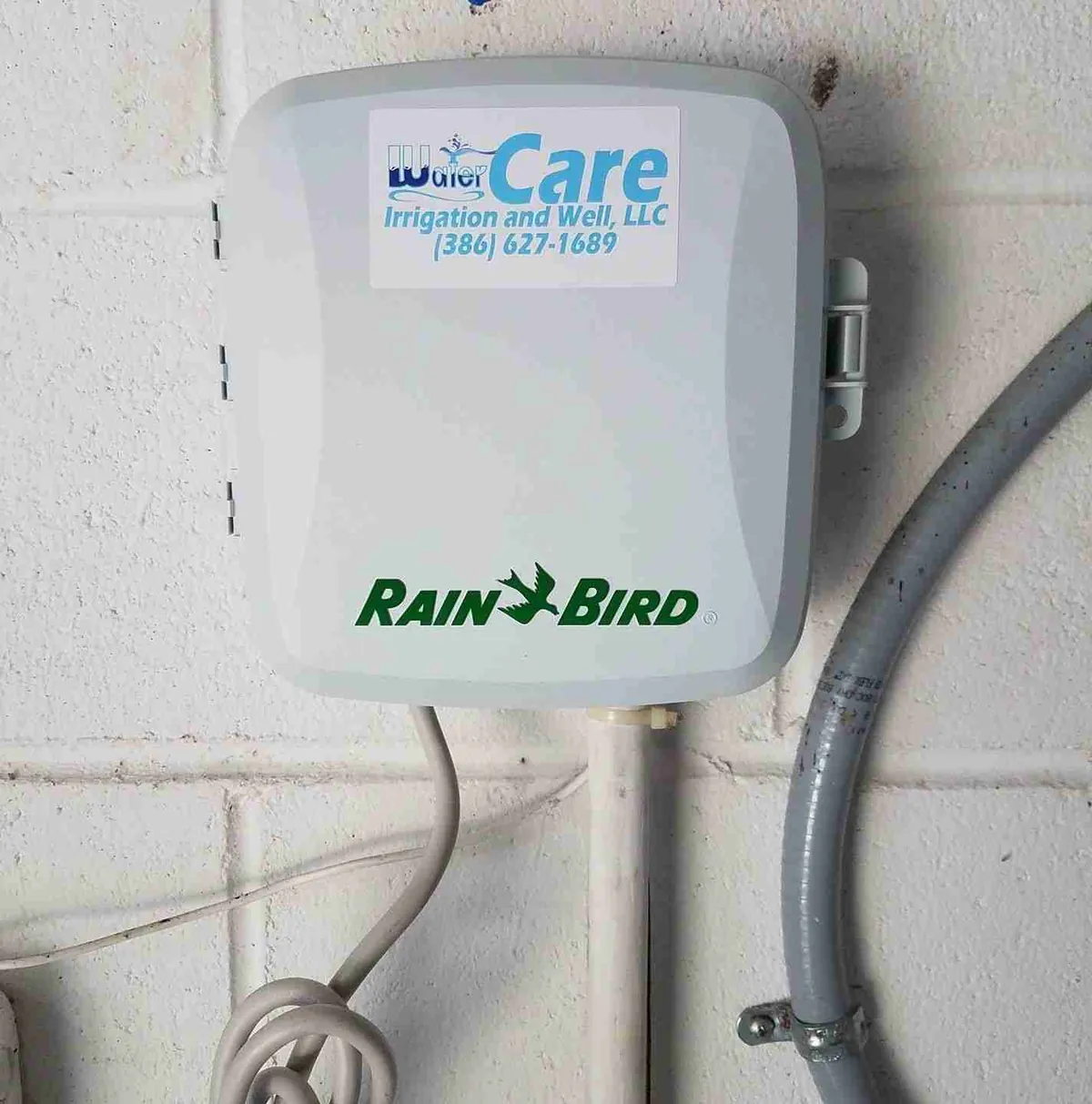 Rain Bird irrigation controller installed on a wall with protected conduit and a WaterCare service label