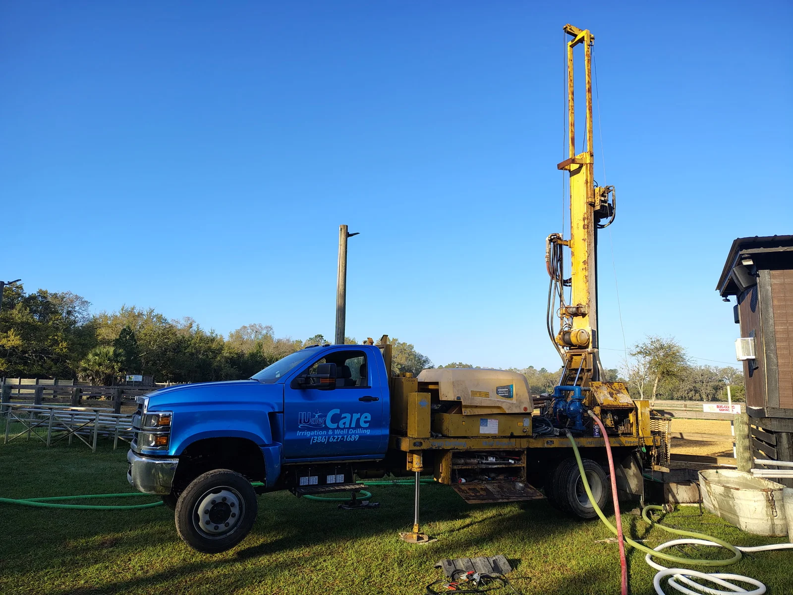 WaterCare well drilling truck set up with outriggers and hoses on a large property
